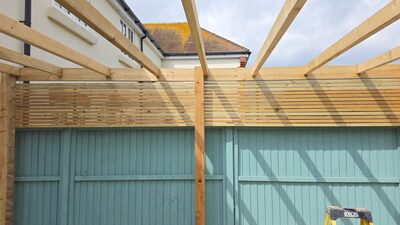 Slatted privacy screen and pergola above painted fence by A Sterling Landscapes